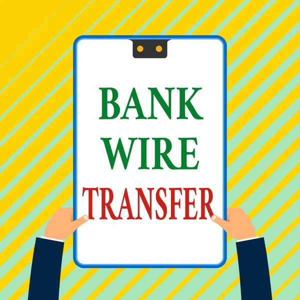 Writing note showing Bank Wire Transfer. Business photo showcasing Electronic transfer of money through bank to bank White rectangle clipboard with blue frame has two holes holds by hands.