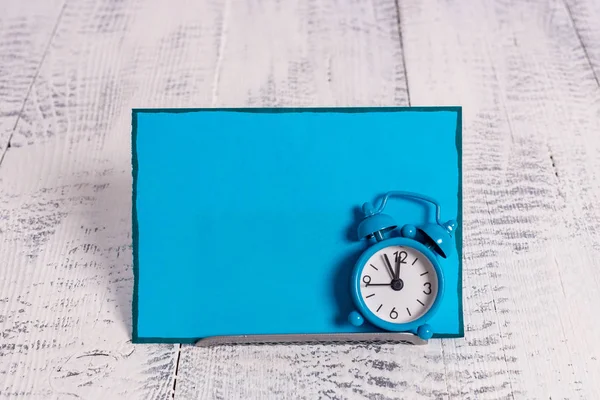 Mini blauwe kleur wekker om te laten zien tijd geplaatst gekanteld in de voorkant van een blauwe briefpapier. Klassiek horloge boven een bufferdraad voor notatiepapier — Stockfoto