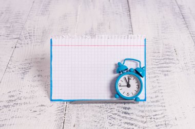 Mini mavi alarm saati beyaz bir not kağıdının önüne yerleştirilmiş zamanı gösterir. Simge kablosunun üzerinde duran klasik küçük saat gösterim kağıdının önünde
