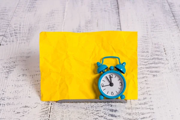 Mini blauwe kleur wekker om te laten zien tijd geplaatst gekanteld voor een gele briefpapier. Klassiek horloge boven een bufferdraad voor notatiepapier — Stockfoto