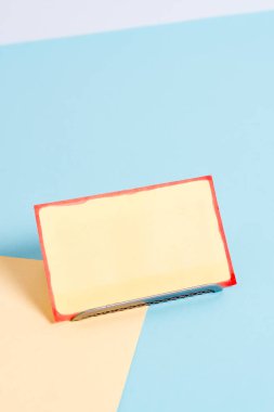 Paper sheet placed tilted on a buffer wire with a soft pastel backdrop. Notepaper on the edge of empty plain multi colours table. Artistic way of arranging flat lays photography