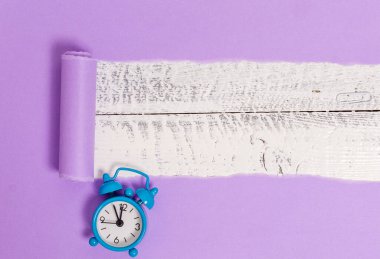 Tahta klasik bir masanın üzerine küçük bir çalar saat yerleştirilmiş. Ahşap bir arka planda kalın yırtık bir kağıt. Dairenin sanatsal düzenleme yöntemi fotoğrafçılıktır.