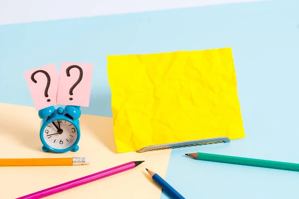 Mini reloj despertador de pequeño tamaño junto a estacionario colocado inclinado. Notepaper en el borde de la mesa vacía multicolor llano telón de fondo. Manera artística de organizar planos pone fotografía — Foto de Stock