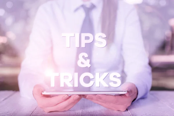 Handwriting text writing Tips And Tricks. Concept meaning Steps Lifehacks Handy advice Recommendations Skills Female business person sitting by table and holding mobile phone.
