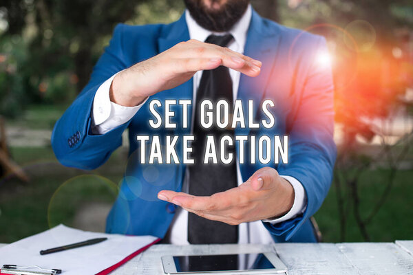 Conceptual hand writing showing Set Goals Take Action. Business photo showcasing Act on a specific and clearly laid out plans Man in front of table. Mobile phone and notes on the table.