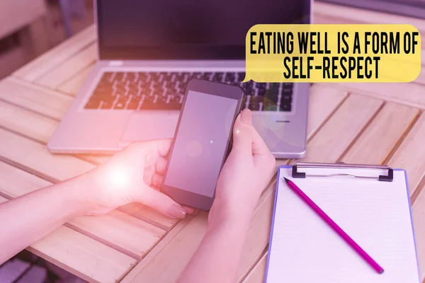 Tekst pisma "Dobrze się odżywiać" jest formą szacunku dla samego siebie. Koncepcja oznacza cytat promowania zdrowego stylu życia kobieta laptop smartphone biuro dostarcza urządzeń technologicznych. — Zdjęcie stockowe