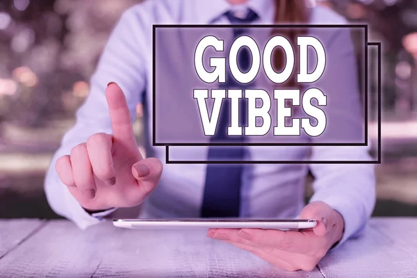 Text sign showing Good Vibes. Conceptual photo slang phrase for the positive feelings given off by a demonstrating Female business person sitting by table and holding mobile phone.