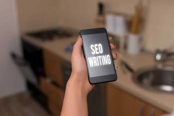 Conceptual hand writing showing Seo Writing. Business photo text grabbing the attention of the search engines using specific word woman using smartphone and technological devices inside the home.