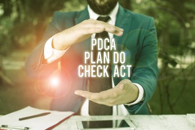 Conceptual hand writing showing Pdca Plan Do Check Act. Business photo showcasing Deming Wheel improved Process in Resolving Problems Man in front of table. Mobile phone and notes on the table.