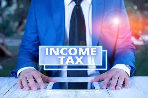 Writing note showing Income Tax. Business photo showcasing Annual charge levied on both earned and unearned income Businessman in blue suite with a tie holds lap top in hands. — Stock Photo, Image