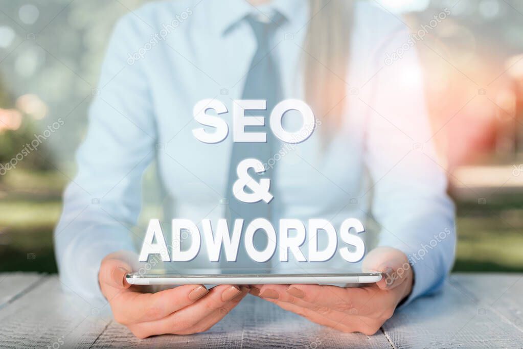 Handwriting text writing Seo And Adwords. Concept meaning Pay per click Digital marketing Google Adsense Female business person sitting by table and holding mobile phone.