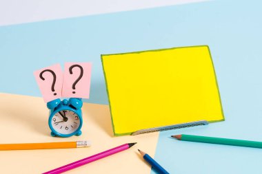 Sabit konuma getirilmiş mini küçük çalar saat. Boş sade çok renkli masa arkaplanının kenarındaki not kağıdı. Dairenin sanatsal düzenleme yöntemi fotoğrafçılıktır.