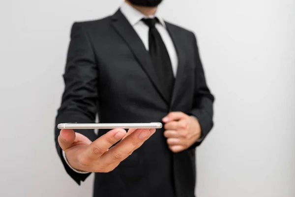 Man människa med skägg bära formella arbetskläder hålla högteknologiska smartphone-enhet. Man klädd i arbetskläder plus slips håller liten mobil hi tech telefon med en hand — Stockfoto