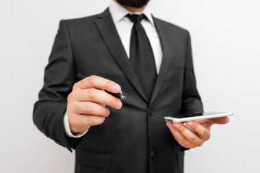 Sakallı bir erkek resmi iş kıyafetleri giyer yüksek teknoloji akıllı telefon cihazı taşır. İş elbisesi giymiş bir adam ve kravatlı küçük cep telefonlu bir adam tek elini kullanıyor.