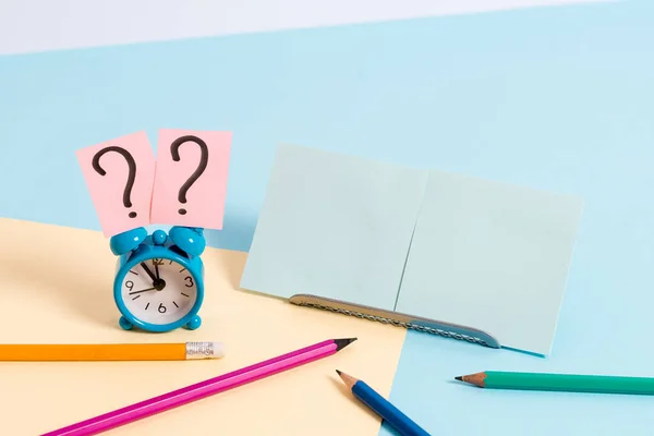 Mini reloj despertador de pequeño tamaño junto a estacionario colocado inclinado. Notepaper en el borde de la mesa vacía multicolor llano telón de fondo. Manera artística de organizar planos pone fotografía — Foto de Stock