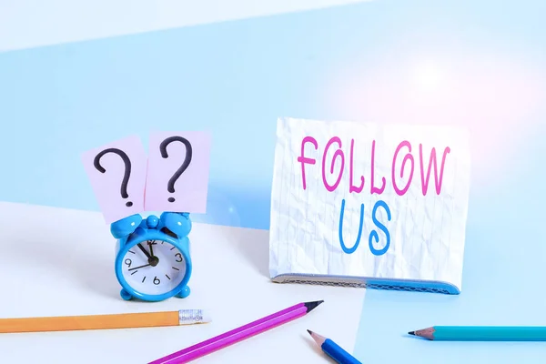 Writing note showing Follow Us. Business photo showcasing To invite a demonstrating or group to join his company and take rules Mini size alarm clock beside stationary on pastel backdrop.