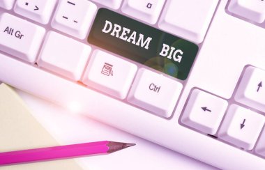 Dream Big 'i gösteren bir not yazıyorum. Hayatınız için amaç arayan bir iş fotoğrafı gösterimi ve beyaz arkaplanının üzerinde nota kağıdıyla birlikte beyaz bilgisayar klavyesinde gerçekleştirilme işlemi.