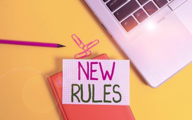 Writing note showing New Rules. Business photo showcasing recently one of a set of explicit or understood regulations Laptop clips pencil paper sheet hard cover notebook colored background. clipart