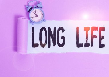 Text sign showing Long Life. Conceptual photo able to continue working for longer than others of the same kind Alarm clock and torn cardboard placed above plain pastel table backdrop.