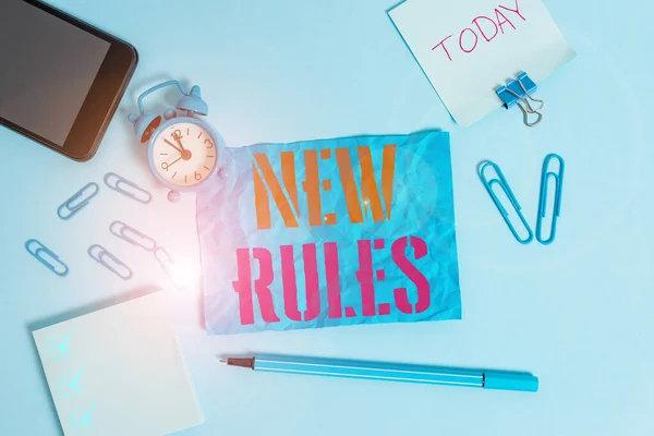 Word writing text New Rules. Business concept for recently one of a set of explicit or understood regulations Alarm clock clips notepad smartphone rubber band marker colored background.