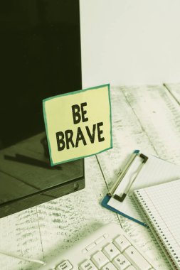 Text sign showing Be Brave. Conceptual photo ready to face and endure danger or pain showing courage Bold Note paper taped to black computer screen near keyboard and stationary.