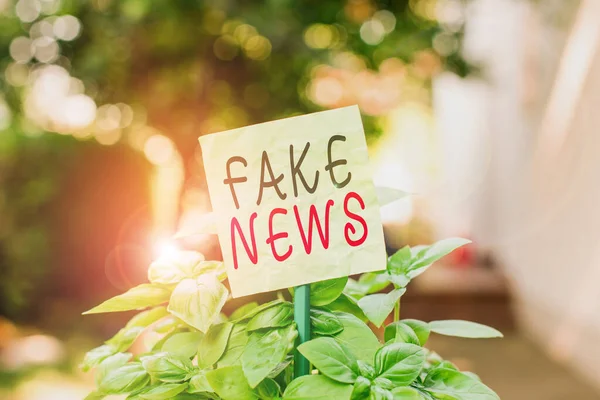 Text sign showing Fake News. Conceptual photo Giving information to showing that is not true by the media Plain empty paper attached to a stick and placed in the green leafy plants.