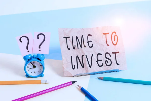 Conceptual hand writing showing Time To Invest. Business photo showcasing Creation of capital capable of producing other goods Mini size alarm clock beside stationary on pastel backdrop. — Stock Photo, Image