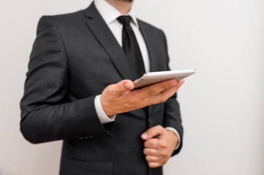 Sakallı bir erkek resmi iş kıyafetleri giyer yüksek teknoloji akıllı telefon cihazı taşır. İş elbisesi giymiş bir adam ve kravatlı küçük cep telefonlu bir adam tek elini kullanıyor.