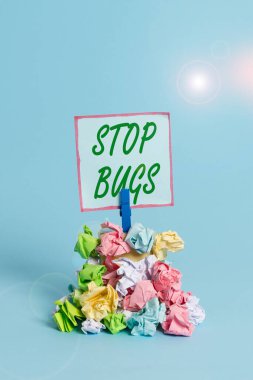 Handwriting text Stop Bugs. Concept meaning Get rid an insect or similar small creature that sucks blood Reminder pile colored crumpled paper clothespin reminder blue background.