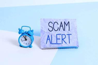 El yazısı yazıları Scam Alert. Kavram demek, birini dolandırıcılık ya da entrika hakkında uyarmak demek. Pastel arka plana yaslanmış kağıdın yanında olağandışı bir Mini çalar saat..