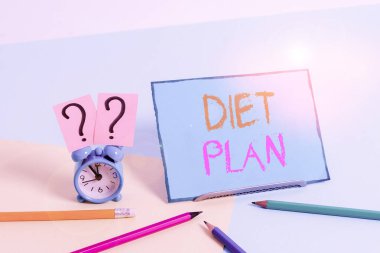 Diyet Planı 'nı gösteren bir not yazıyorum. İş fotoğrafı gösterimi, sağlıklı beslenme alışkanlığı edinmek ya da başarmak için ayrıntılı bir teklif sunuyor. Pastel arka planda sabit duran Mini boyunda alarm saati..