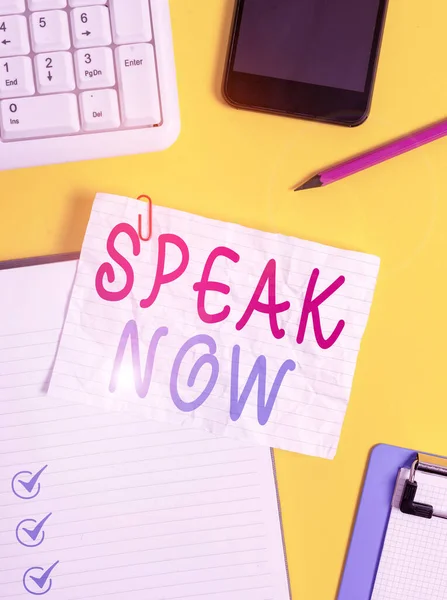 Writing note showing Speak Now. Business photo showcasing Communicate to us your feelings and information Voice out Crumpled white paper on table paper clips clock mobile and pc keyboard.