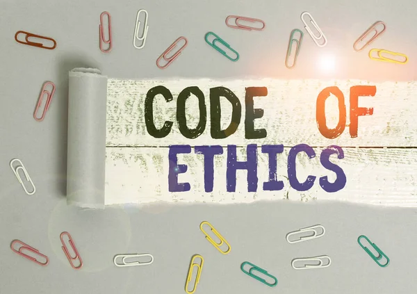 Handwriting text Code Of Ethics. Concept meaning Moral Rules Ethical Integrity Honesty Good procedure Paper clip and torn cardboard placed above a wooden classic table backdrop.
