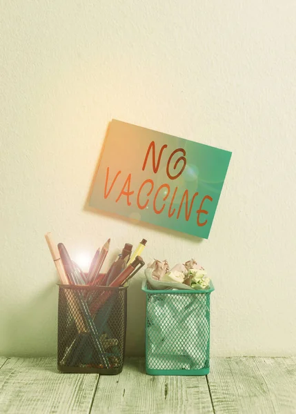 Text sign showing No Vaccine. Conceptual photo not provided of immunity against one or several diseases Blue Sticky Card on Wall Two Pencil Pots Pens Pencils Markers Waste Paper.
