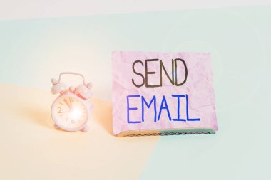 Handwriting text writing Send Email. Concept meaning the system for using computers to send messages over the internet Mini size alarm clock beside a Paper sheet placed tilted on pastel backdrop.