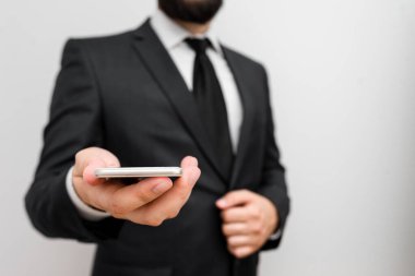 Sakallı bir erkek resmi iş kıyafetleri giyer yüksek teknoloji akıllı telefon cihazı taşır. İş elbisesi giymiş bir adam ve kravatlı küçük cep telefonlu bir adam tek elini kullanıyor.