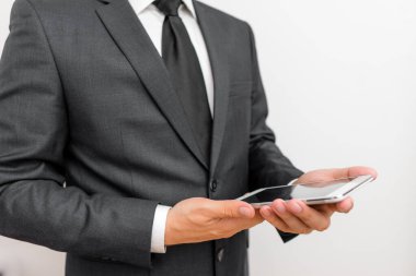 Sakallı bir erkek resmi iş kıyafetleri giyer yüksek teknoloji akıllı telefon cihazı taşır. İş elbisesi ve kravat takmış bir adam iki eliyle cep telefonu tutuyor.