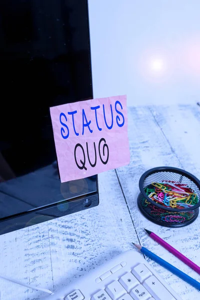 Handwriting text writing Status Quo. Concept meaning existing state of affairs regarding social or political issues Note paper taped to black computer screen near keyboard and stationary.