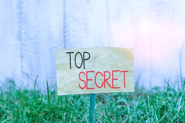 Handwriting text writing Top Secret. Concept meaning protected by a high degree of secrecy Highly confidential Plain empty paper attached to a stick and placed in the green grassy land. — Stockfoto