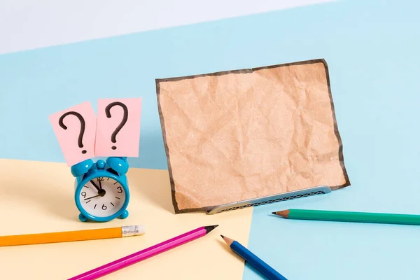 Mini reloj despertador de pequeño tamaño junto a estacionario colocado inclinado. Notepaper en el borde de la mesa vacía multicolor llano telón de fondo. Manera artística de organizar planos pone fotografía — Foto de Stock