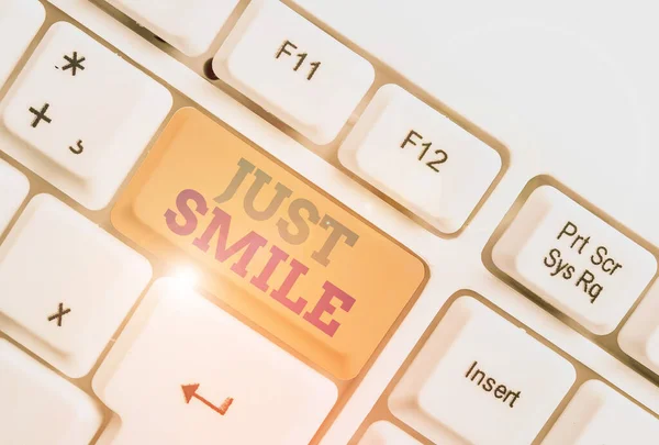 Handschrift tekst schrijven Just Smile. Concept betekent veronderstellen een gezichtsuitdrukking die plezier of amusement aangeeft Witte pc toetsenbord met lege nota papier boven witte achtergrond sleutel kopieerruimte. — Stockfoto