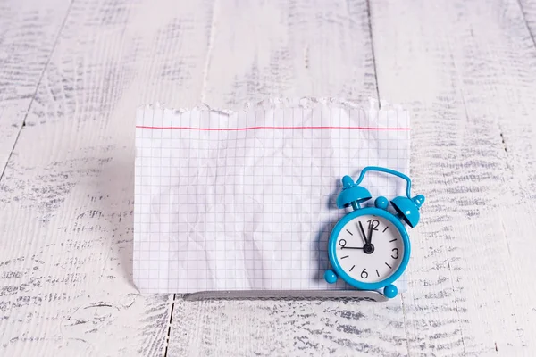 Mini sveglia a colori blu per mostrare il tempo posizionato inclinato di fronte a un notepaper bianco. Classico piccolo orologio in piedi sopra un filo tampone davanti alla carta notazione — Foto Stock