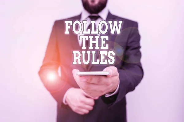 Text sign showing Follow The Rules. Conceptual photo order someone stick to certain place country guides stricts Male human wear formal work suit hold smart hi tech smartphone use one hand. — Stock Photo, Image