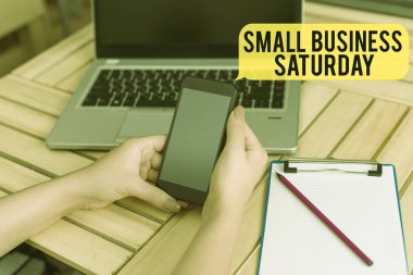 Cumartesi günü Küçük İşletme el yazısı. Konsept, Amerikan alışveriş tatili anlamına geliyor. Dizüstü bilgisayarlı bilgisayar bilgisayar ofisi, teknolojik cihazları tedarik ediyor..