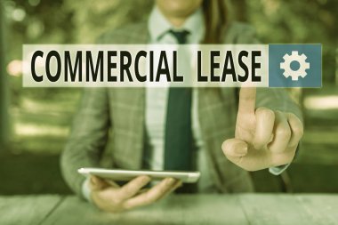 Conceptual hand writing showing Commercial Lease. Business photo showcasing contract between a landlord and a business property tenants Female business person sitting by table holding mobile phone. clipart