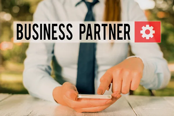 Conceptual hand writing showing Business Partner. Business photo showcasing commercial entity with which another commercial entity Female business person sitting and holding mobile phone.