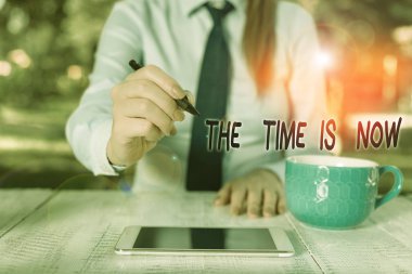 Word writing text The Time Is Now. Business concept for encouraging someone to start doing today Dont be late Business woman sitting by the table with cup of coffee and mobile phone.
