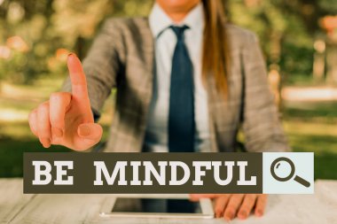 Text sign showing Be Mindful. Conceptual photo paying close attention to or being conscious of something Female business person sitting by table holding mobile phone.