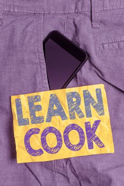 Aşçıyı Öğren 'i gösteren bir not yazıyorum. İş fotoğrafı gösterimi bilgi edinme ya da yemek pişirme becerileri kazanma. Pantolonun içindeki akıllı telefon cihazı ön cep kağıdı kağıdı..