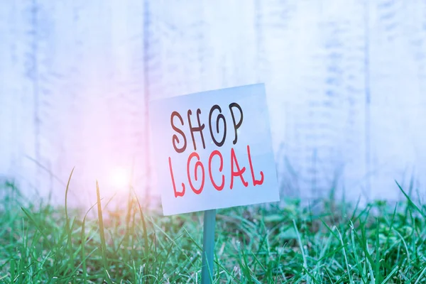 Text sign showing Shop Local. Conceptual photo a preference to buy locally produced goods and services Plain empty paper attached to a stick and placed in the green grassy land. — Stock Photo, Image